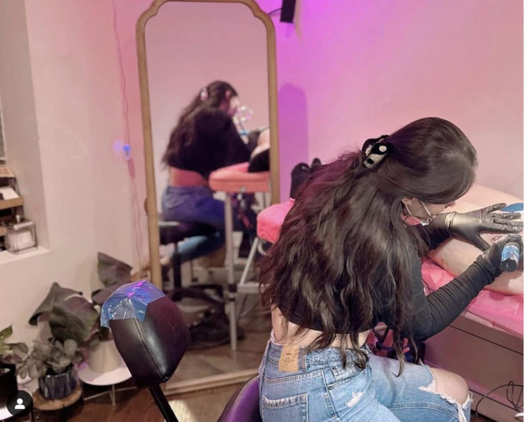 woman tattooing someone in a pink interior of crispy aura studio