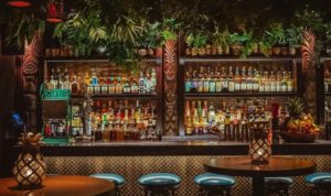 Bar interior shows tiki style decor with a full hightop counter and leather stools