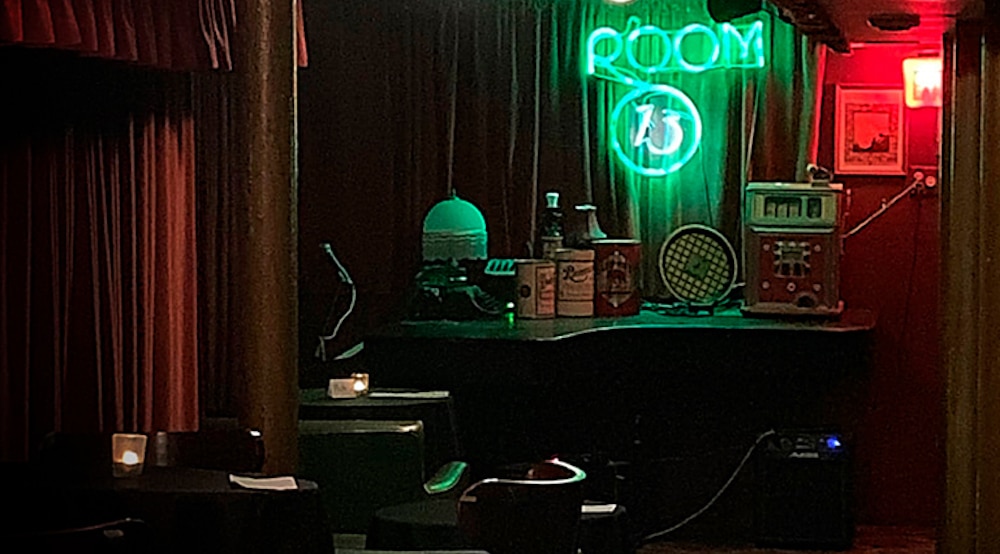 a room with a neon green sign displaying room 13 with red flooring a pink florescent light 