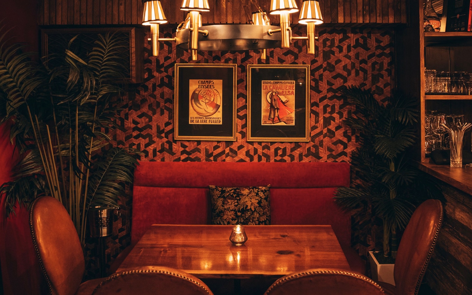 cocktail bar with a light hanging and a velvet red booth with four leather chairs around a wooden table with two pictures hanging on the wall 