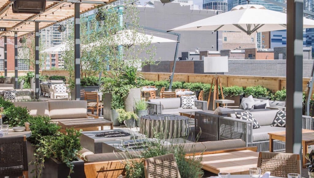 Image of Aba rooftop with a tons of green plants in between the tables with lounging couches and firepits