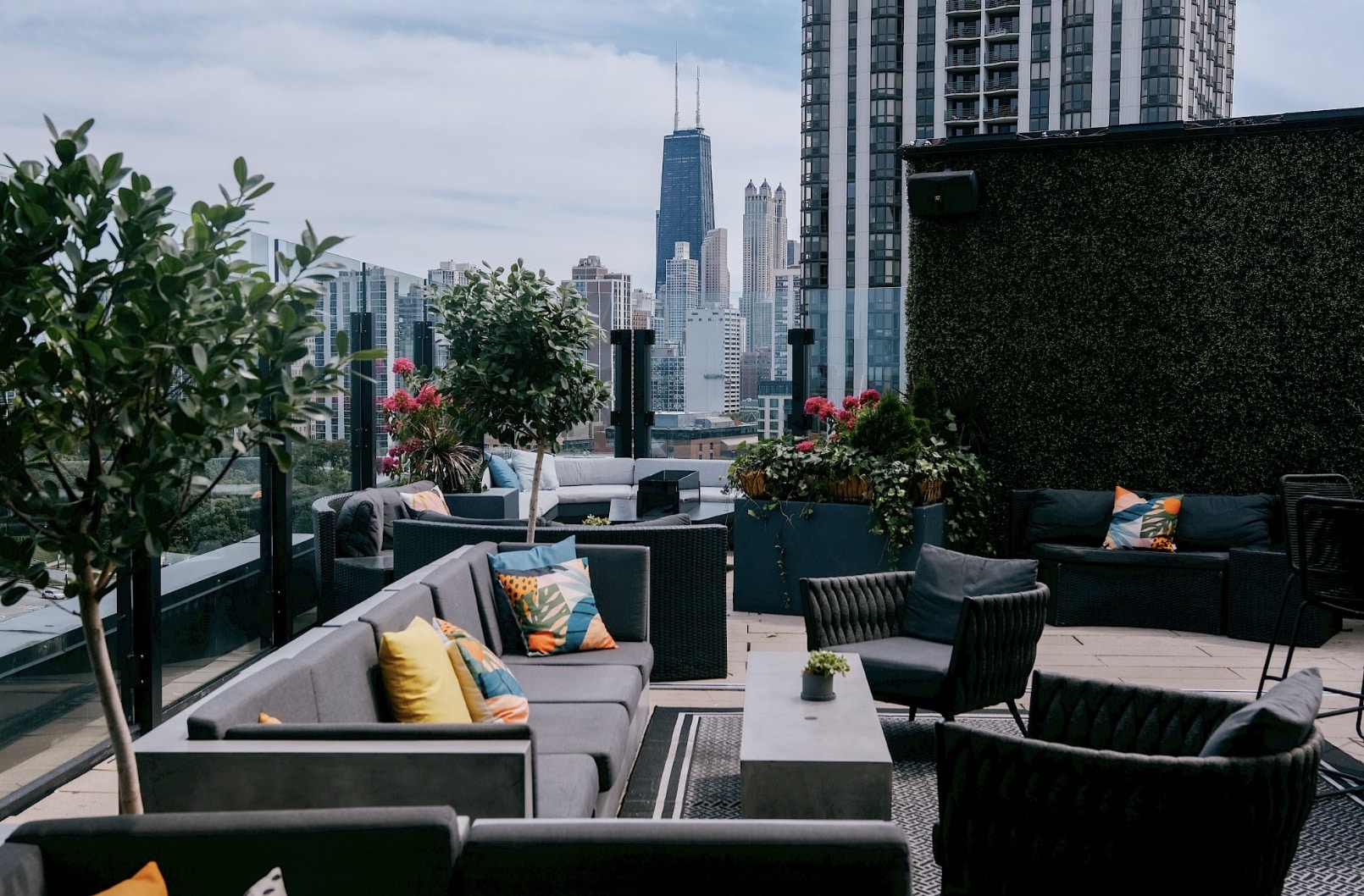 J parker rooftop with tree , flowers, couches with blue, orange, yellow pillows views of the john hancock and the four seasons
