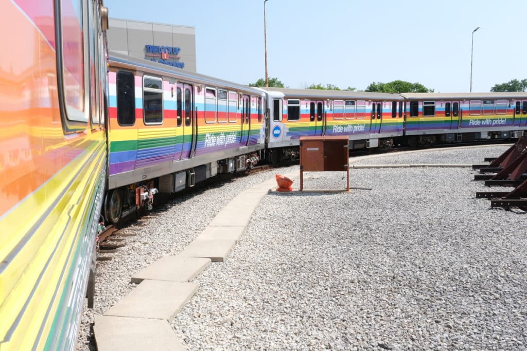 Image showing the CTA's 2023 Pride Train with the rainbow flag covering 8-cars of a train riding the Red Line through Fall.