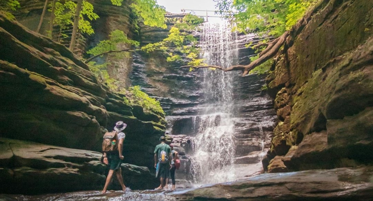 A group of hikers passing under a waterfall at Matthessen State Park in Illinois
