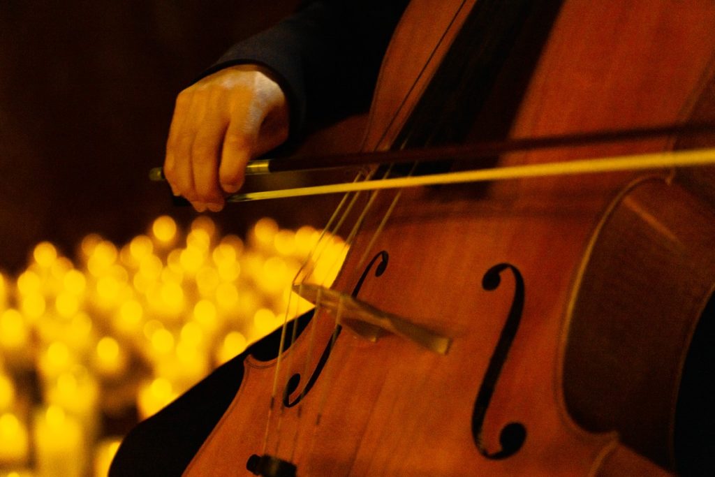 A close-up of a cello with candles in the background