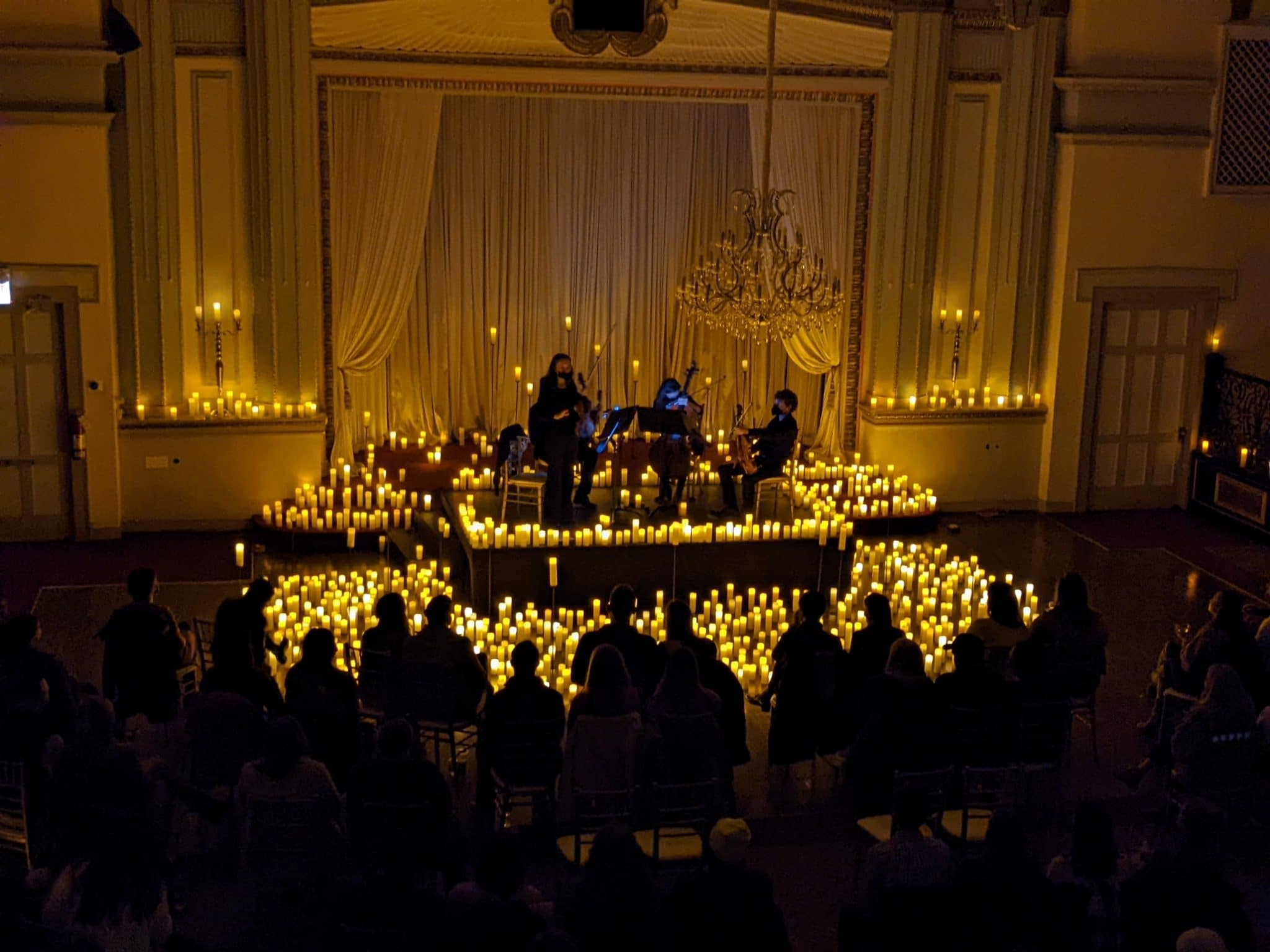 A string quartet performing on a stage at Stan Mansion surrounded by candles.