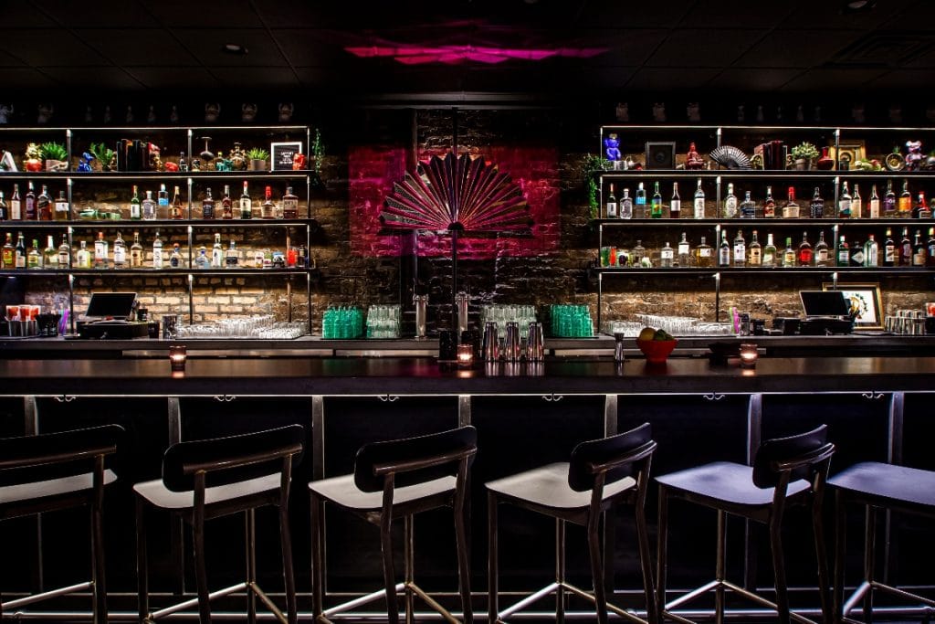 this speakeasy chicago nine bar has a bar counter top pictured with bar stools and stacked shelves