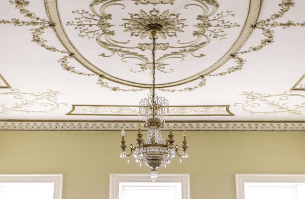 Ceiling of a regency style room with light fixture and golden accents
