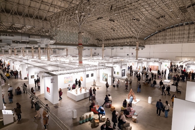 Wide image of the expo room shows visitors and art on the walls