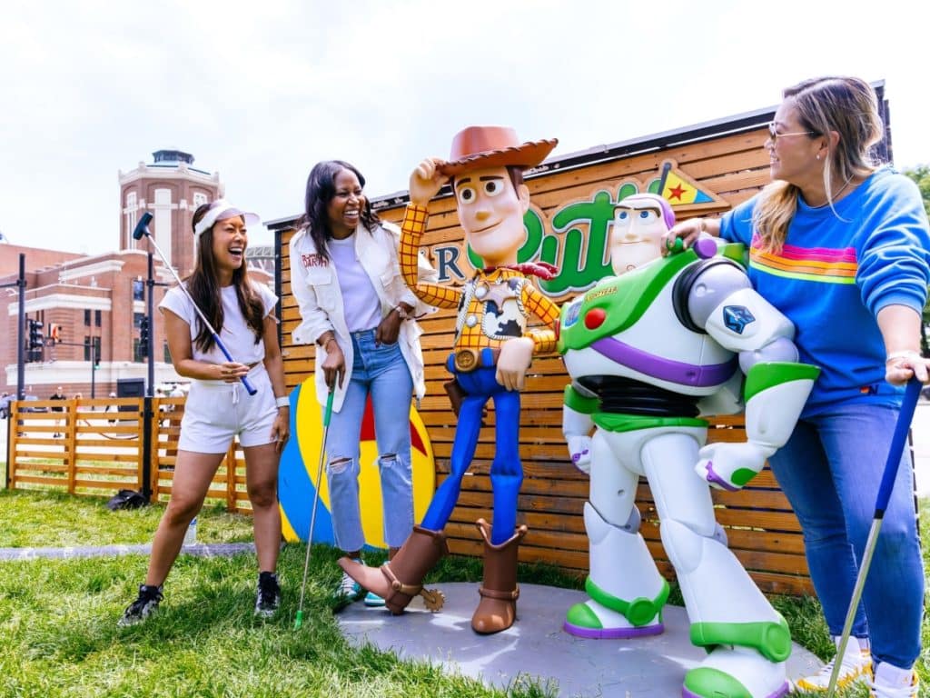 Three friends standing with Toy Story characters at Pixar Putt