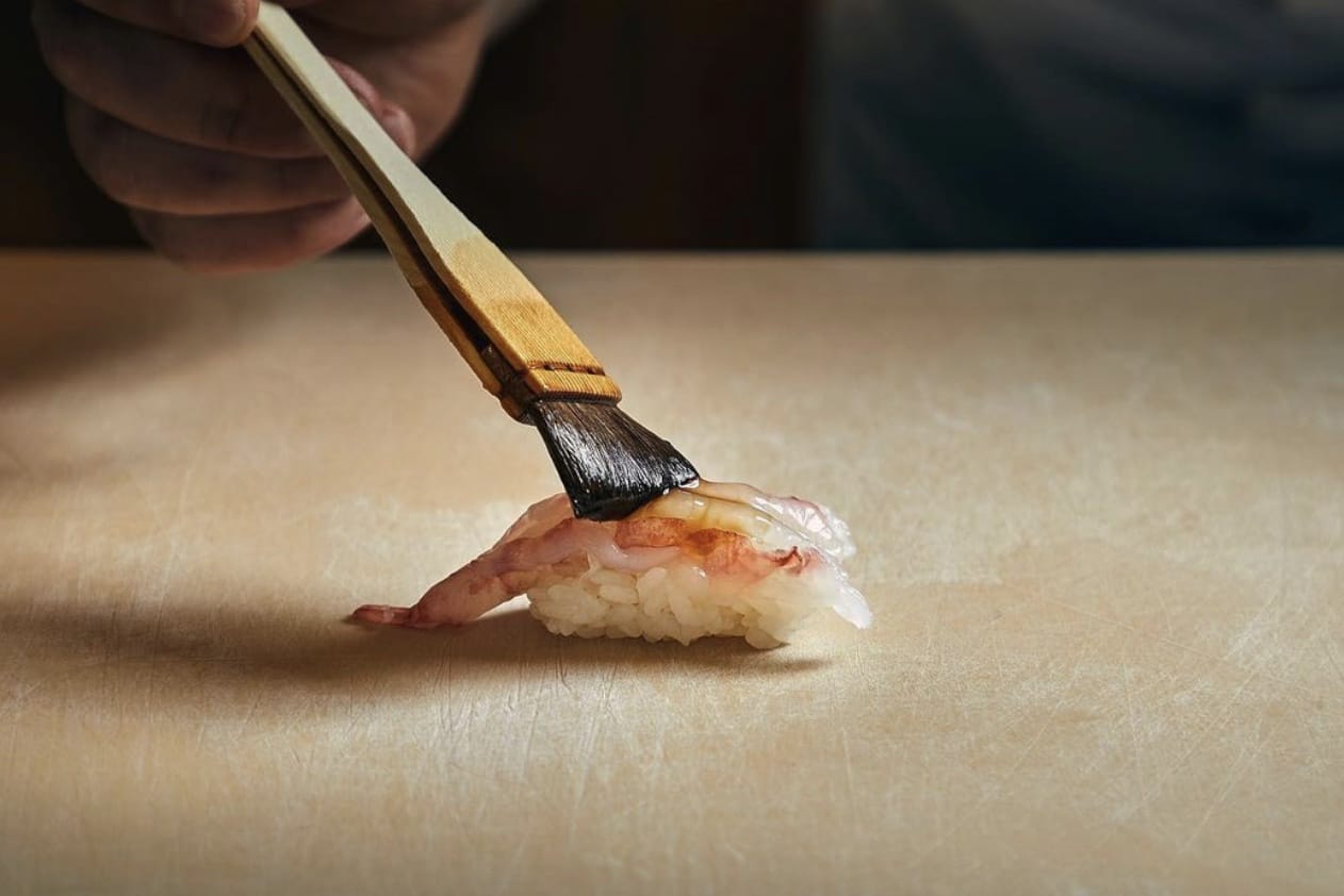 someone using a paint brush to put sauce on a nigiri roll from omakase yume