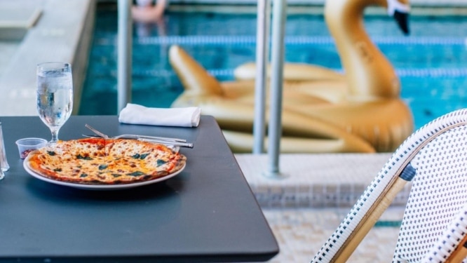 Pizza seen on a table with indoor pool in the background