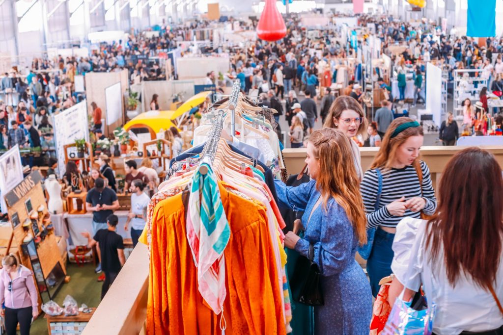 a women wearing a blue dress looking through vintage clothes next to a large group of people during the renegade craft market show 