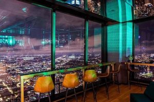 View of the city through the windows of Cloud Bar with bar seats and a table also pictured