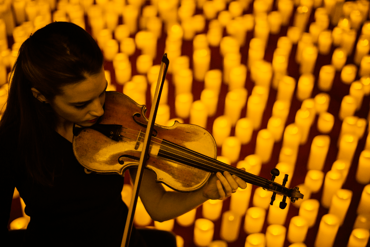 A woman playing the violin with hundreds of candles behind her.