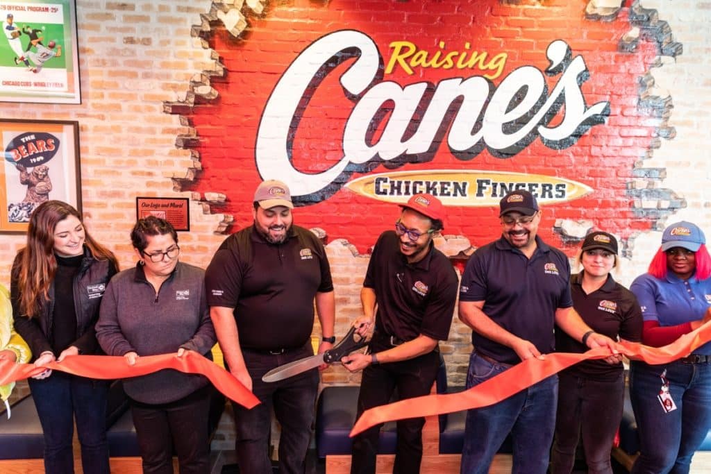 Raising Cane's downtown Chicago location shows employees cutting a ribbon in front of a Cane's sign