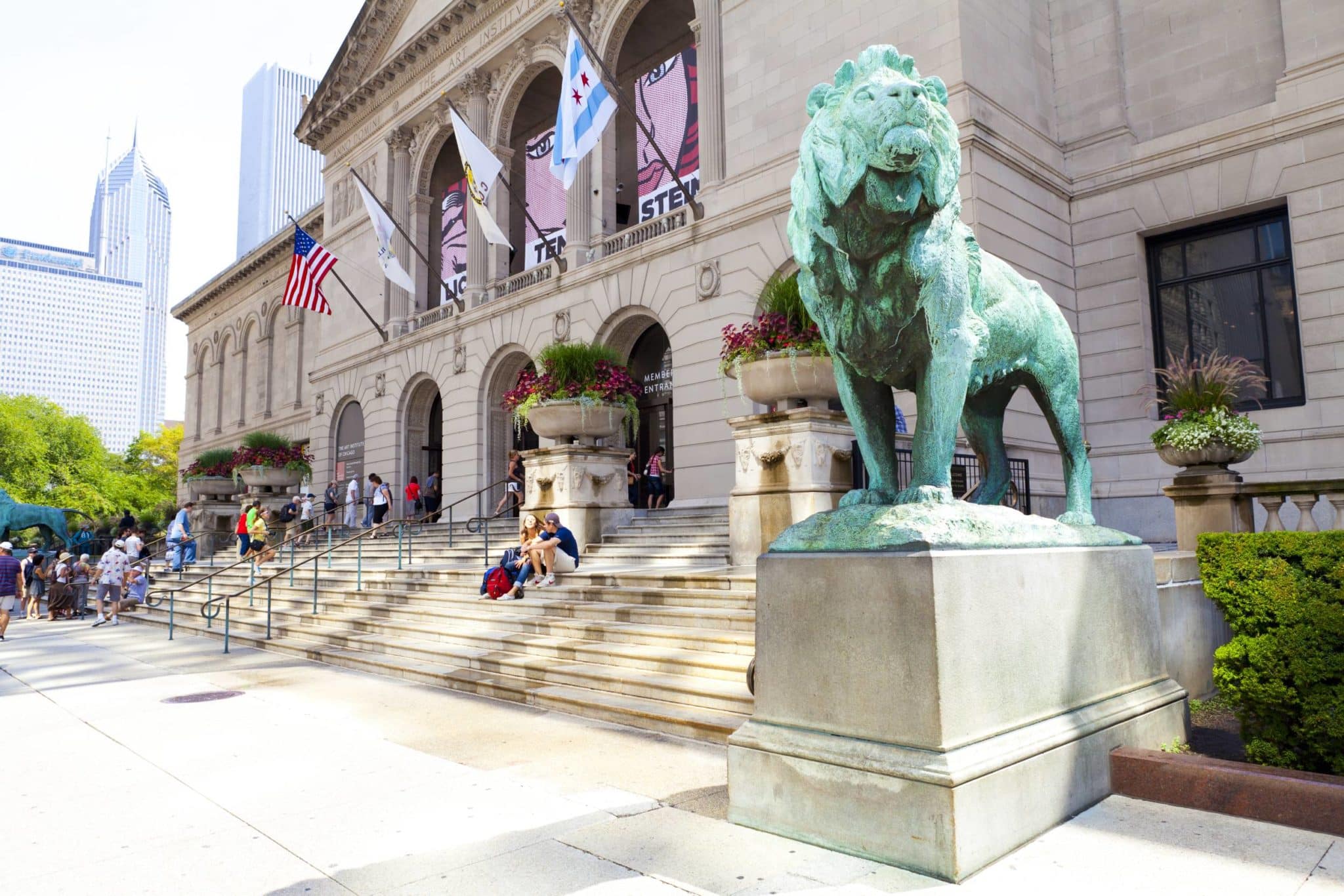 lions outside concrete building with american and chicago flags at art institute of chicago with people of the steps