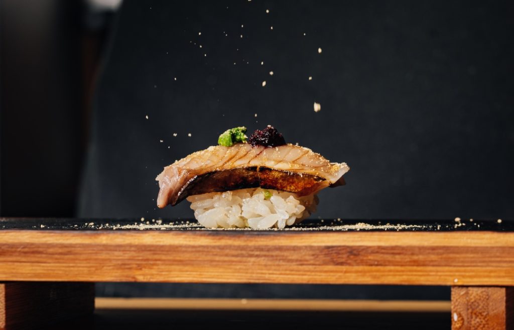 Food prepared by a chef shows fresh fish and rice on a wooden platter