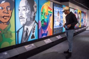 Dark Testament: A Century of Black Writers on Justice exhibit shows colorful depictions of Black Writers; person viewing the exhibit