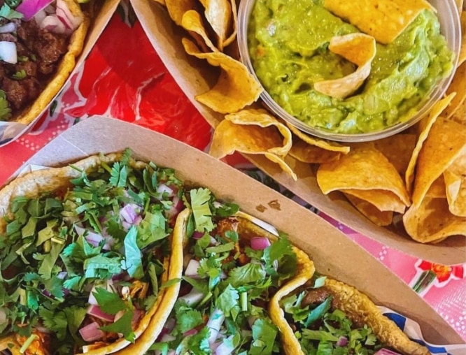 Tacos pictured next to a plate of chips and guacamole
