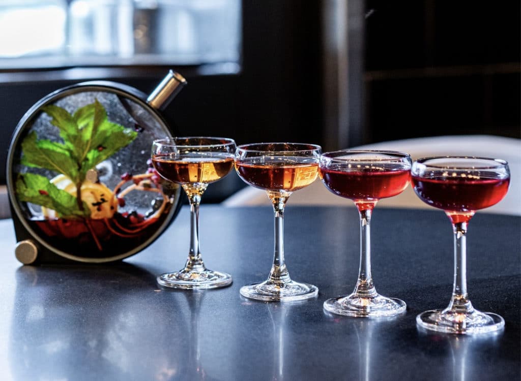 four glasses with red liquor next to a planetarium inspired cocktail bottle