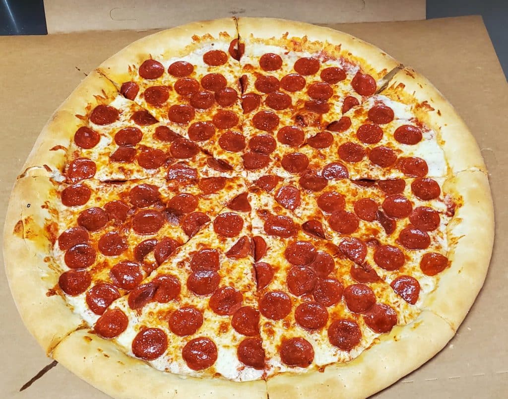 Large pepperoni pizza on a wooden table with melting cheese