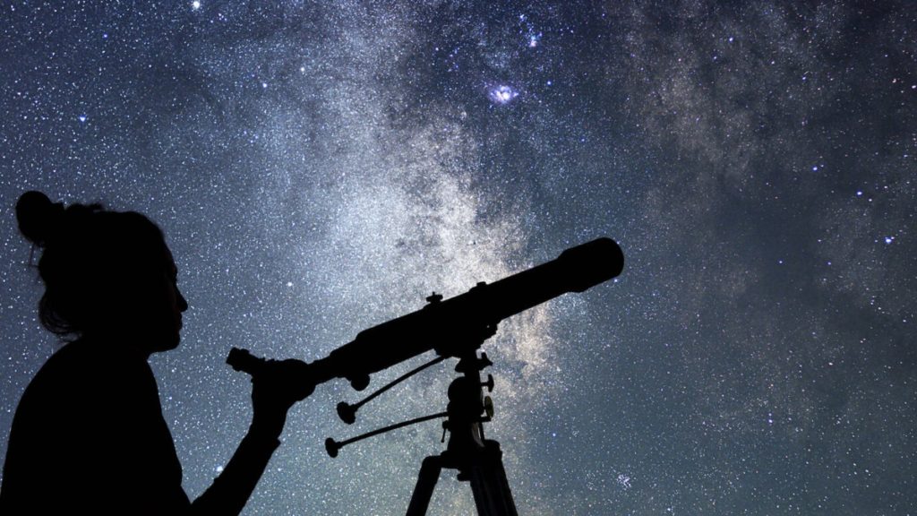 Person looking up at the night sky with a telescope