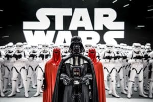 Darth Vader stands with troops in front of the Star Wars logo