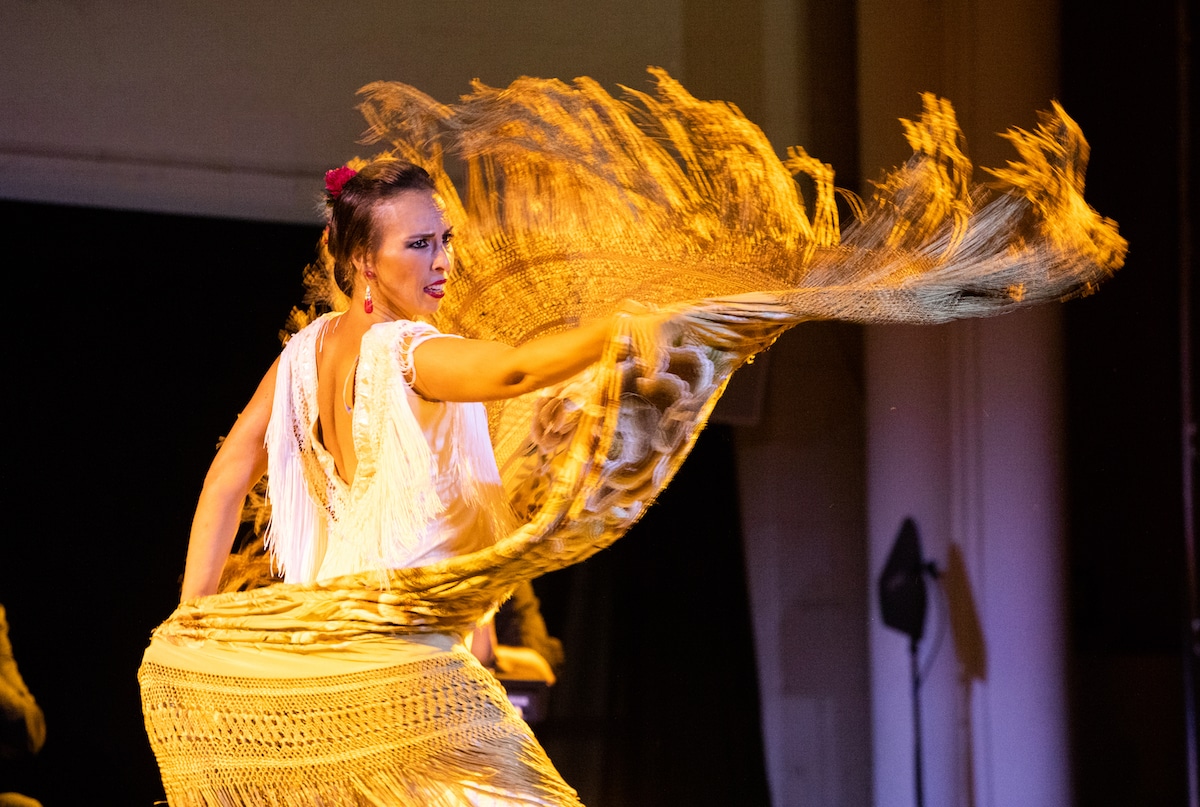 Women with her hair in a bun and wearing a yellow dress performing at Authentic Flamenco
