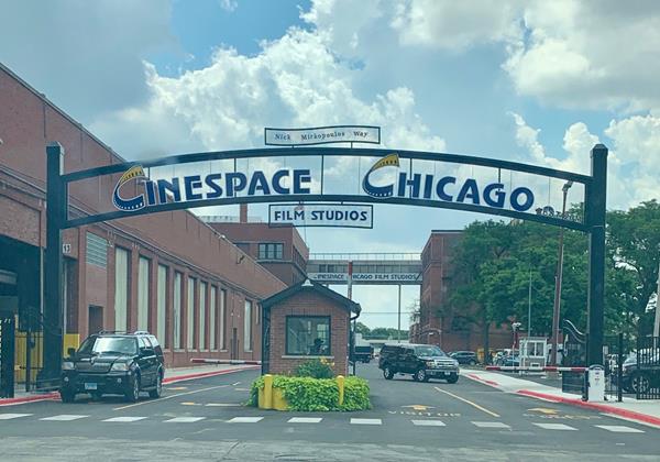 overhead sign of the Cinespace Chicago Film Studios with two cars on the street and trees in the background