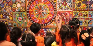 Children pictured standing in front of a colorful textile wall design.