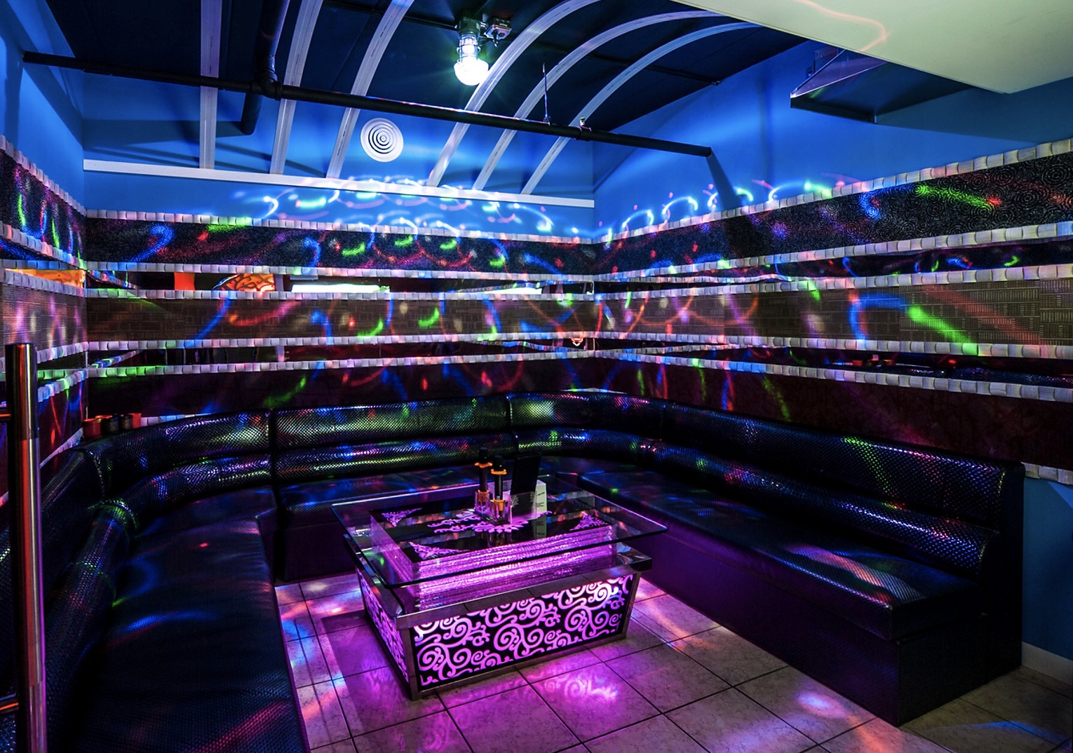 private room at sakura karaoke bar with multicolored lights, a black booth, and table in the center with two microphones