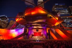 Orchestra performance on the Jay Pritzker Pavilion stage at night with concert attendees seated
