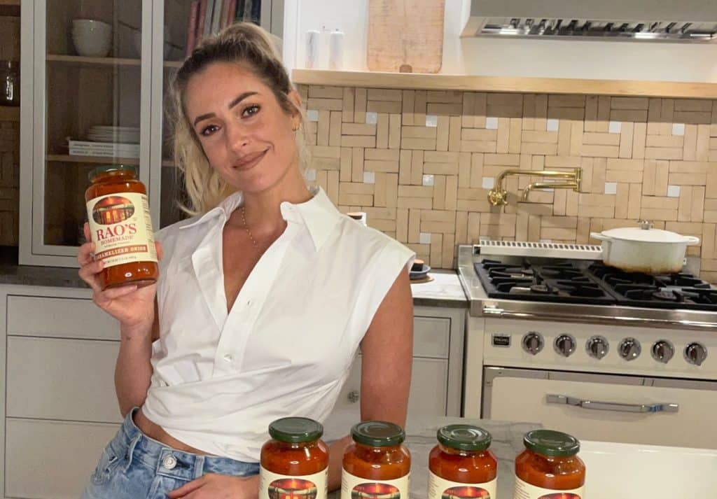 Kristin Cavallari posing in a kitchen holding a jar of Rao’s Homemade sauce