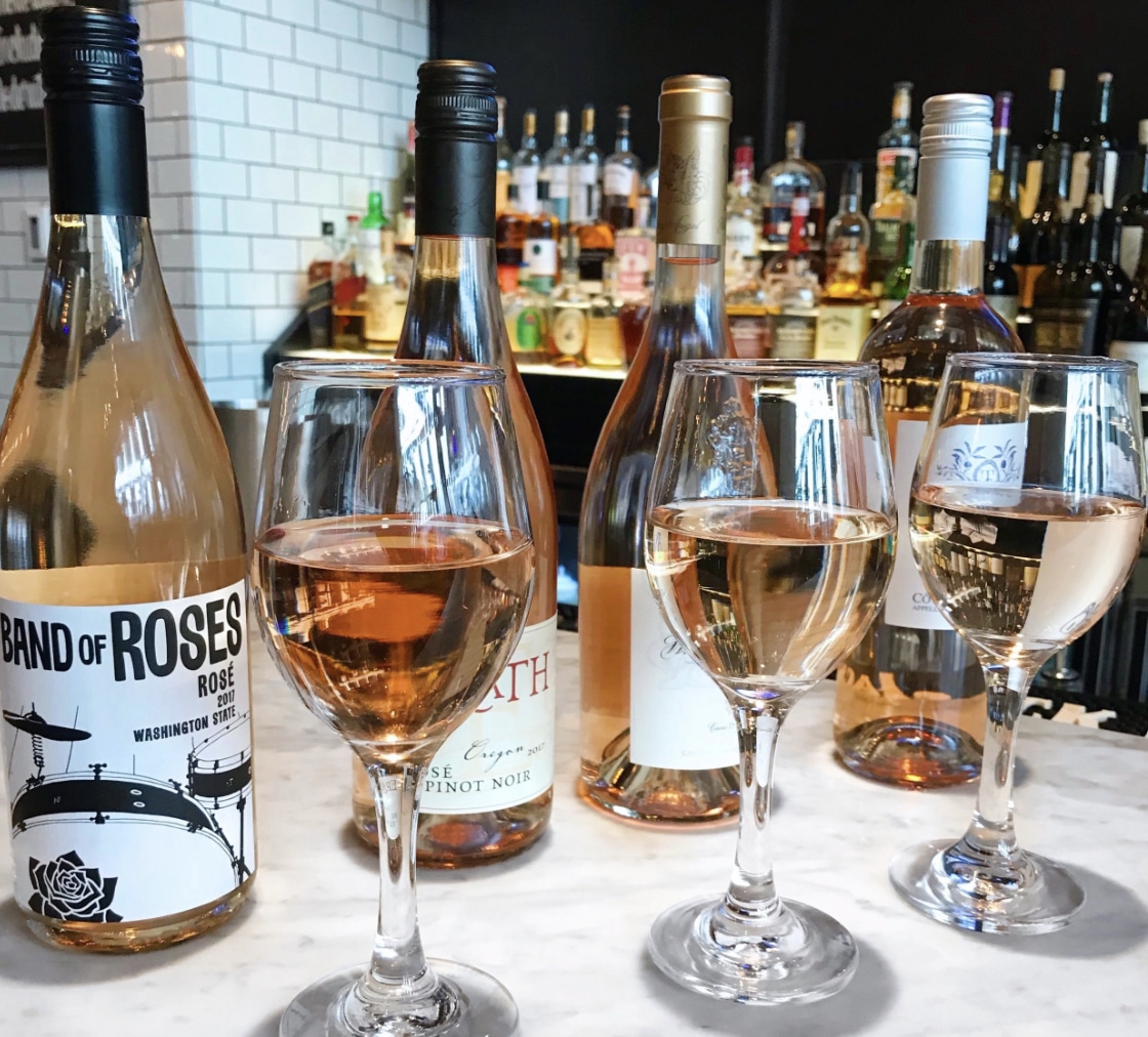 three glass of rose with three different wine bottles, which is included in the happy hour deal, behind on a bar counter at city social