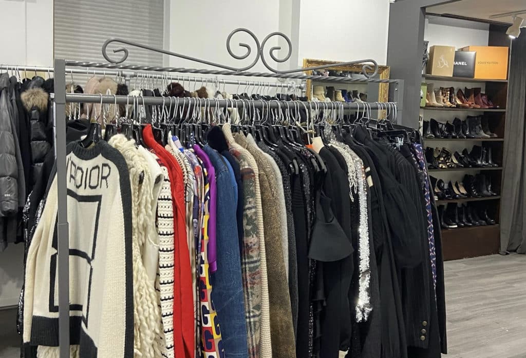 many jackets including a dior jacket hanging on a rack with a stack of shoes in the background at Cynthia's Consignment