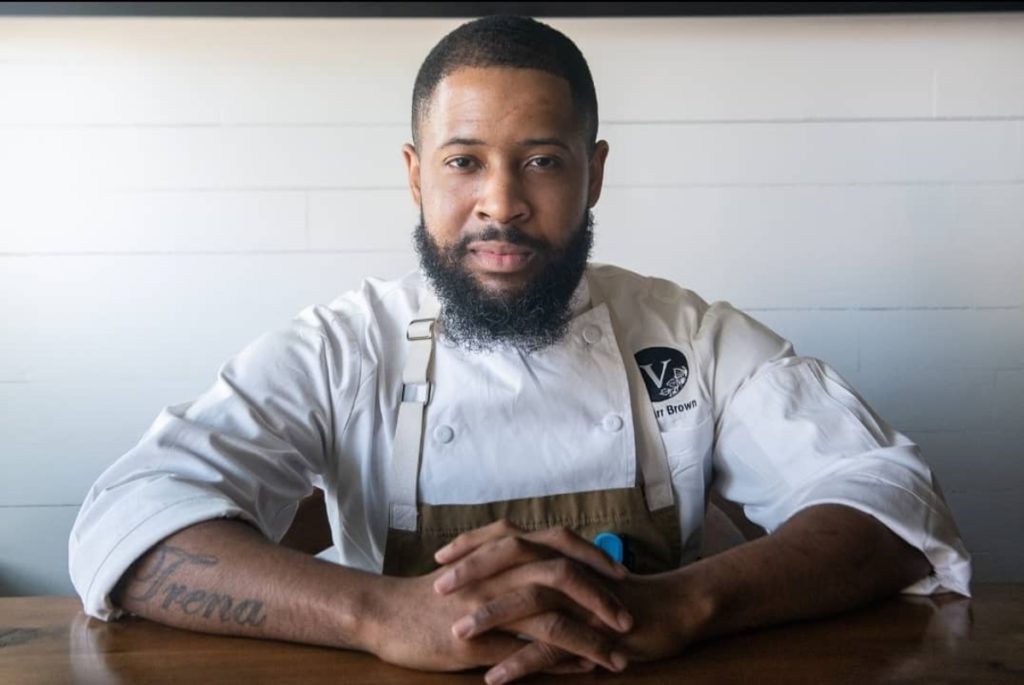 Chef Damarr Brown pictured posing with a neutral expression and his hands in front of him, wearing his chef uniform.