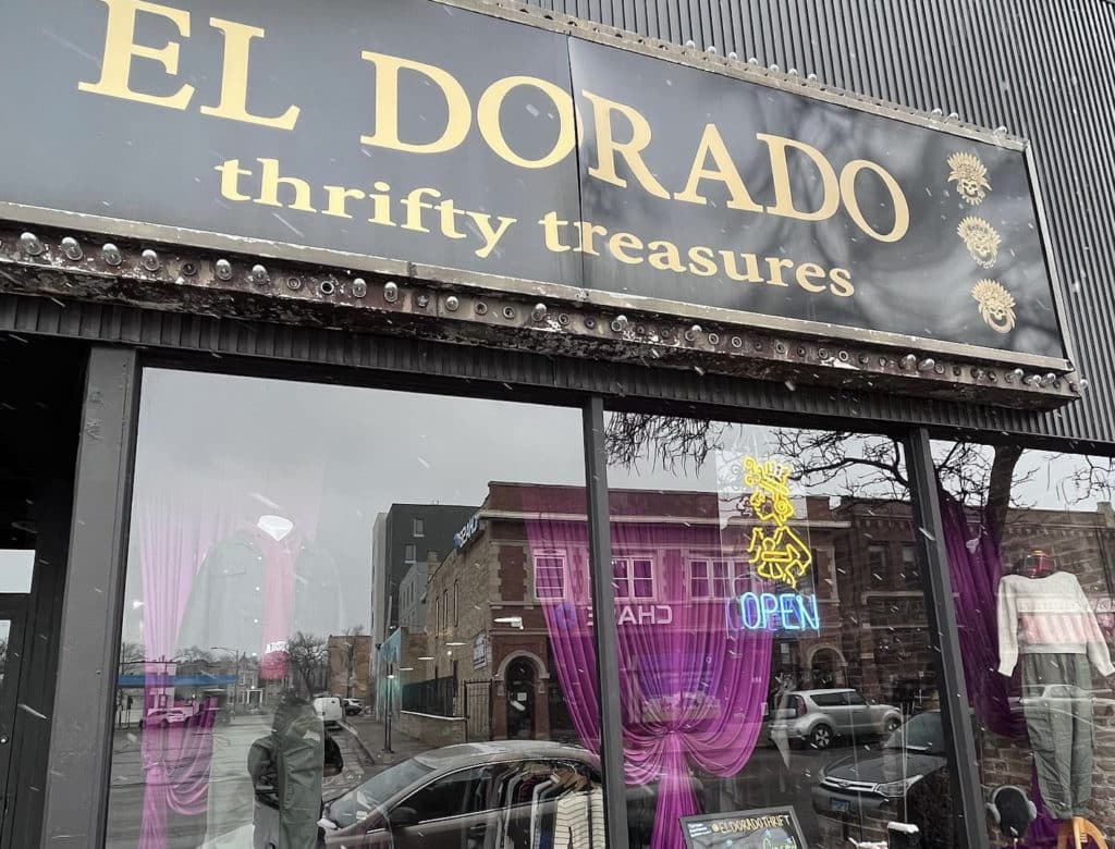 storefront with large yellow letters that say el dorado with a neon sign and clothes behind the glass