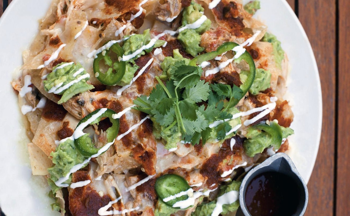 Pulled Chicken Nachos with cilantro and sauce on the side on a white plate, which is the happy hour deal at hub 51
