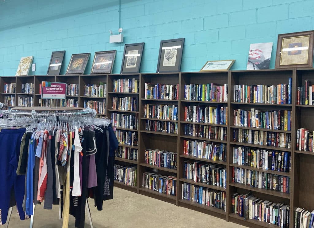 large bookcase of books and cds next to a rack of clothing with pictures on the wall at out of the closet in Chicago
