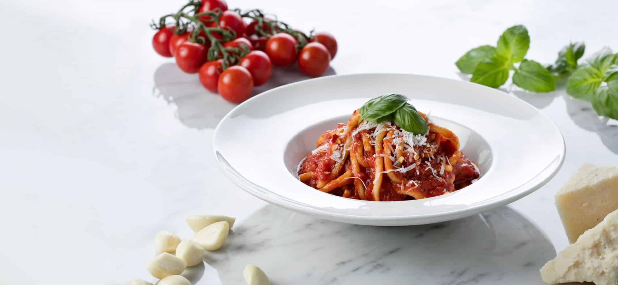angel hair with marinara sauce with basil on a white plate with cherry tomatoes on the side 