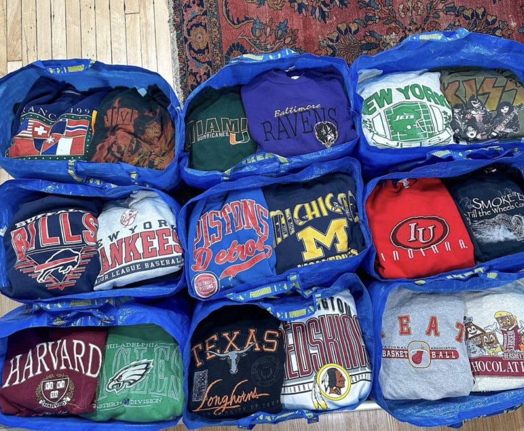 a stack of vintage sweatershirts and shirts in a blue bags of different sports team and colleges at shop life vintage in Chicago