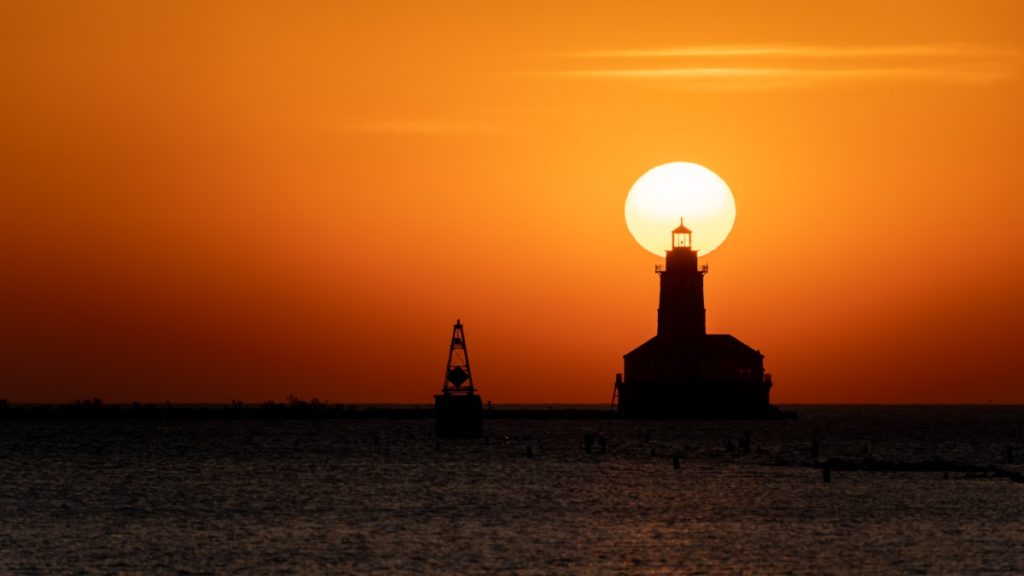 Sun rising behind the Chicago Harbor Lighthouse pictured from Navy Pier