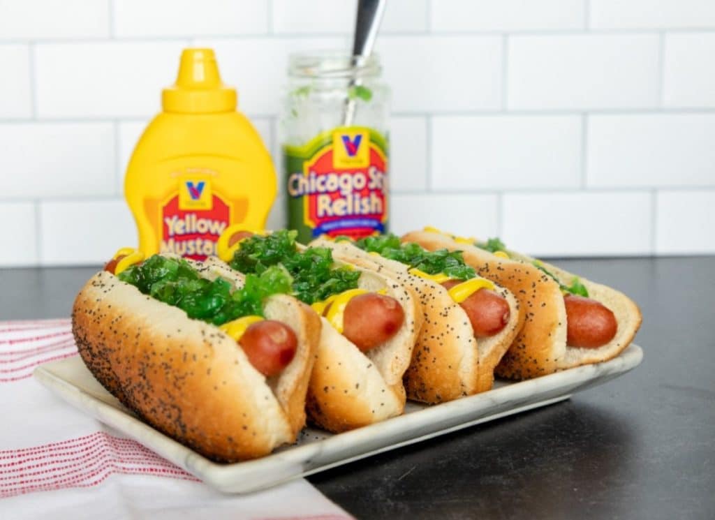 Vienna Beef hotdogs pictured with Chicago-style toppings, and a mustard bottle and relish jar in the background