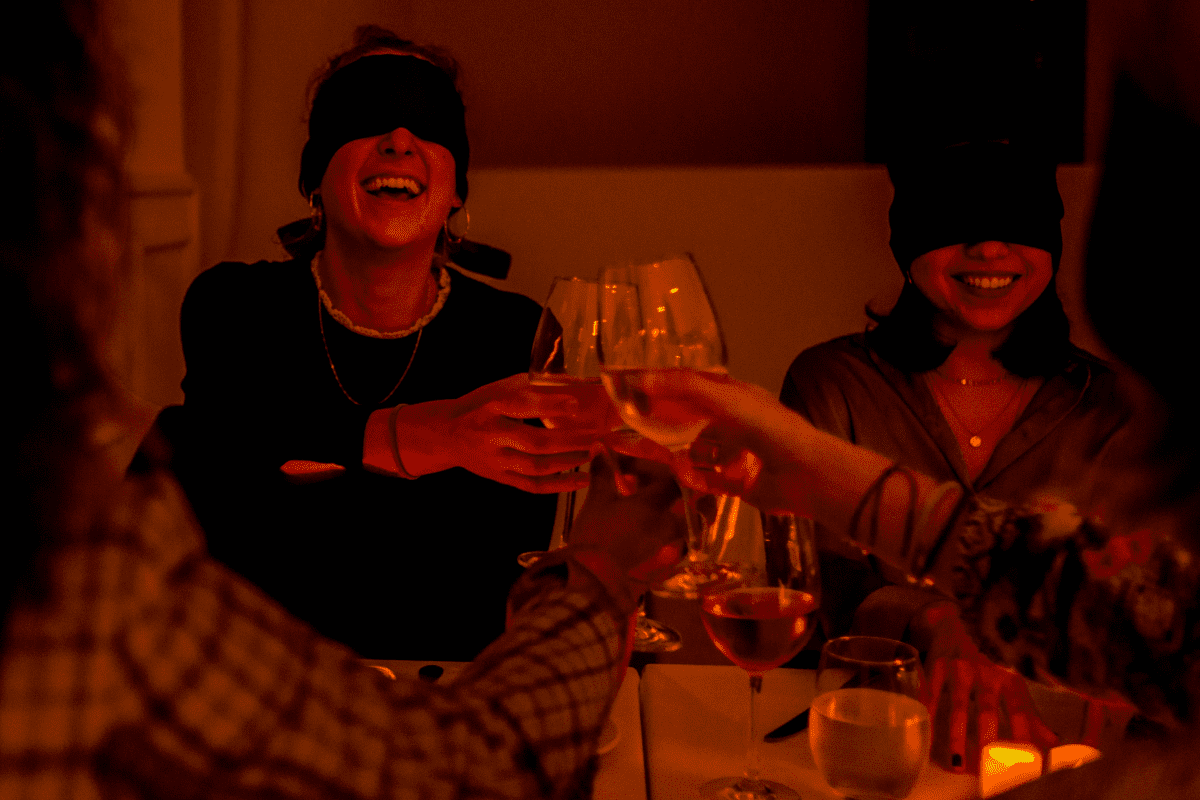 Two women laughing while blindfolded at a Dining in the Dark experience