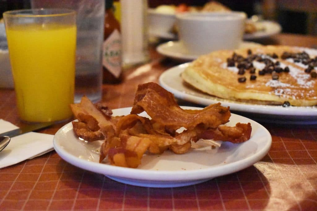 orange juice, bacon, chocolate chip pancakes on a table from sweet maple cafe