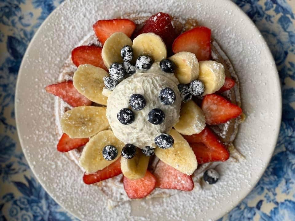  large waffle under strawberries, bananas, and blueberries with ice cream on top.