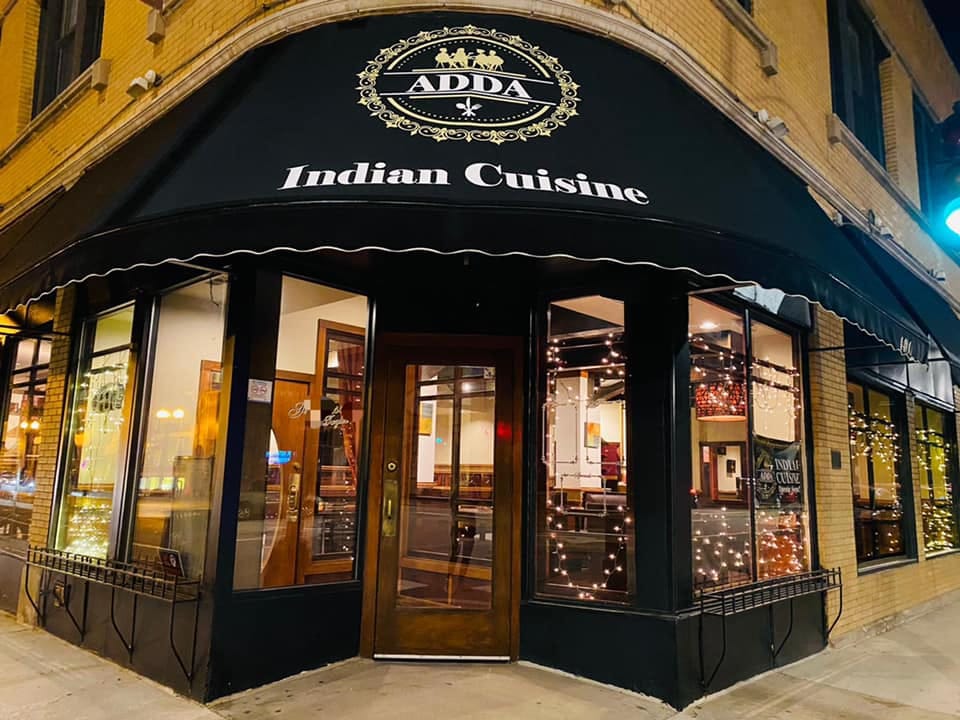 exterior of Adda Indian cuisine with a black covering and glass windows with the lights on in the indian restaurant