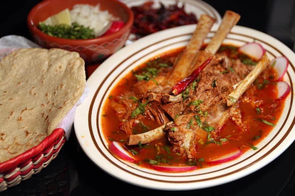 pork sliding off the bone with sauce underneath and parsley on top with tortillas on the side at La Birrieria Restaurant in Chicago