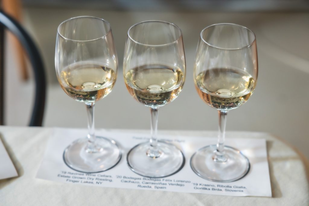 three glasses of white wine on a piece of paper on a concrete table at volo restaurant wine bar in Chicago